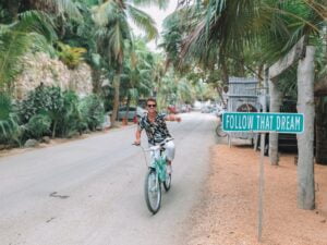 Man ridding bike pointing at a sign that says follow your dream